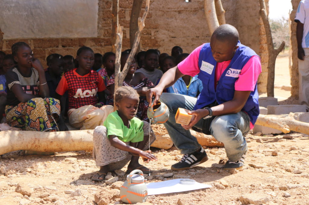 Ett barn i ett flyktingläger lär sig hur man tvättar händerna med stöd av personal från Plan International.