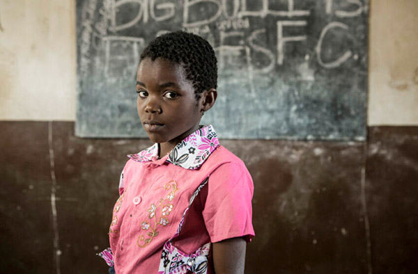 Skolflickan Esnart står framför svarta tavlan i sitt klassrum i Malawi