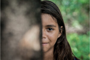 Tjej i Brasilien som döljer halva ansiktet bakom ett träd