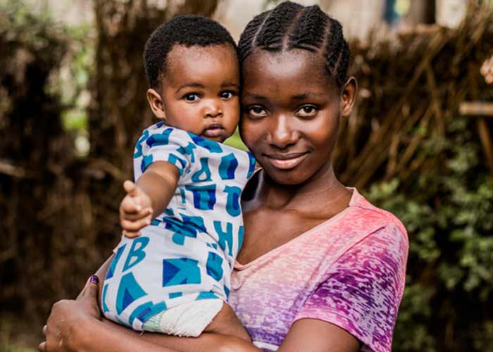 18-åriga Melissa i Zambia tittar in i kameran och håller i sin lilla son som också tittar in i kameran och pekar.