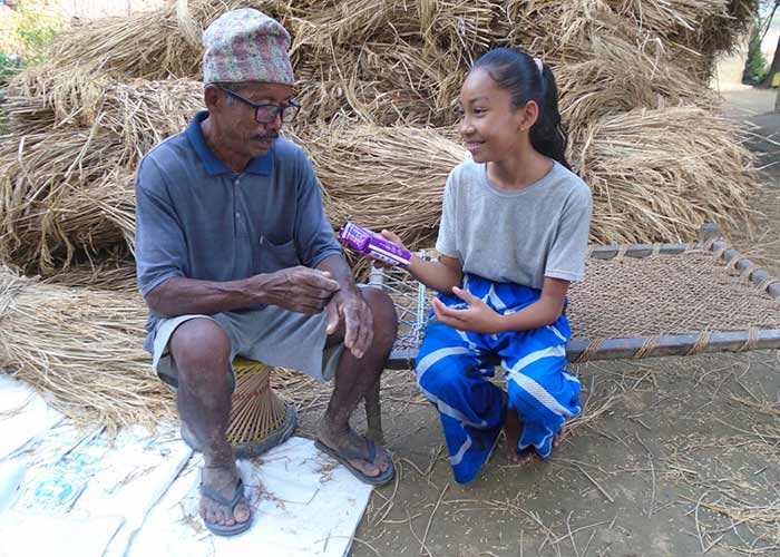 64-åriga Tilakram sitter utomhus i Nepal tillsammans med sitt barnbarn och ger henne ett paket bindor.