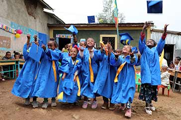 En grupp små skolbarn i Etopien står på gården i sina examenskläder och kastar sina hattar i luften. Utbildning för alla är en av sjutton globala mål för hållbar utveckling.