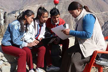 Tre ungdomar i Nepal sitter och tittar på ett papper tillsammans med en ledare. Jämställdhet och inkluderande samhällen är en viktig punkt i de globala målen för hållbar utveckling.