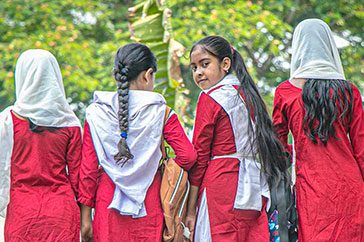 Fyra rödklädda skolflickor med vita sjalar i Bangladesh. Flickors utbildning är en viktig del i vårt projekt Stop the Stigma om mens.
