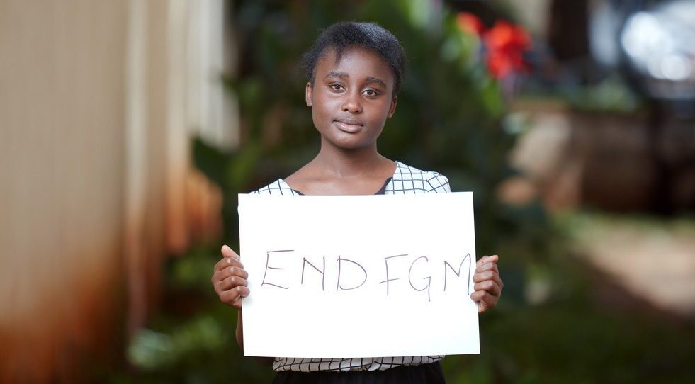 18-åriga Virginia håller upp ett plakat med texten "END FGM"