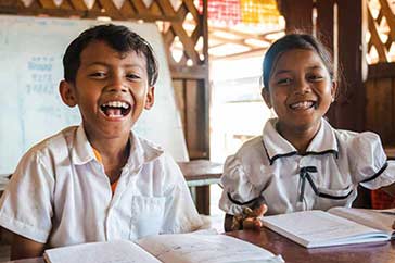 10-åriga Khan och Kruy sitter glada med skolböcker uppslagna på bänken framför dem i klassrummet i