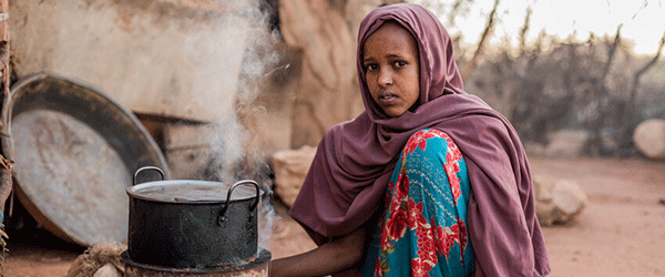 Flicka i Somalia som sitter på marken bredvid en kokande gryta.