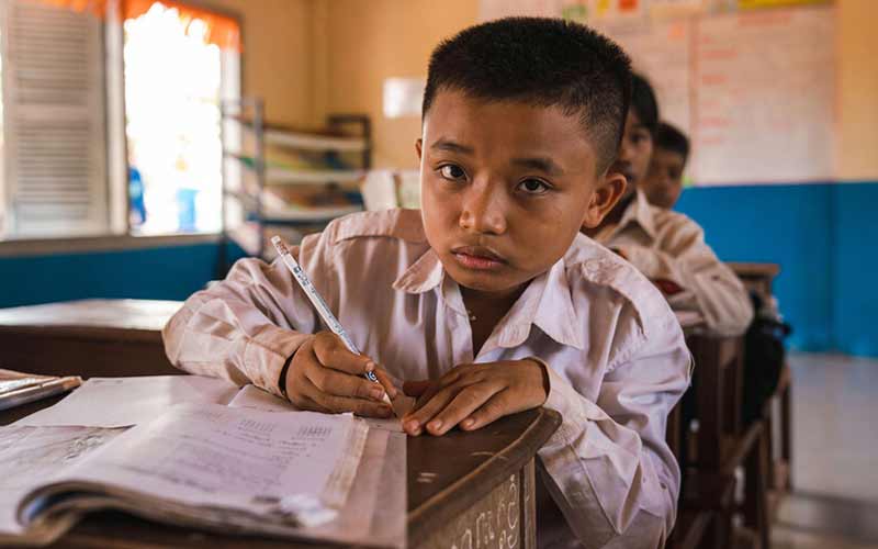 10-åriga Ly Meng Koung sitter och skriver vid sin bänk i klassrummet i Kambodja. Utbildning är avgörande för barns framtid.