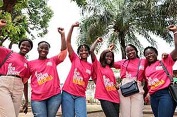 Sex tjejer i rosa tröjor uppmärksammar internationella flickdagen i Guinea-Bissau. De ler och sträcker upp en varsin arm i luften.