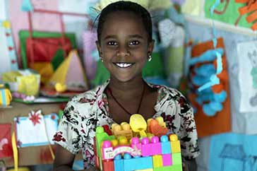 10-åriga Meron ler och visar upp ett hus hon byggt med färgglada klossar. Hon befinner sig på en trygg plats för barn i ett flyktingläger i Tigray, Etiopien. Dessa platser erbjuda skydd mot våld, lek, skolgång och annat som ger barn på flykt en vardag.