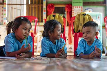 Tre små barn i skolan i Kambodja. De sitter vid ett bord och ritar.