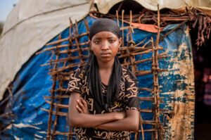 Meron, 11 år, står med armarna i kors utanför sitt hem i Etiopien.