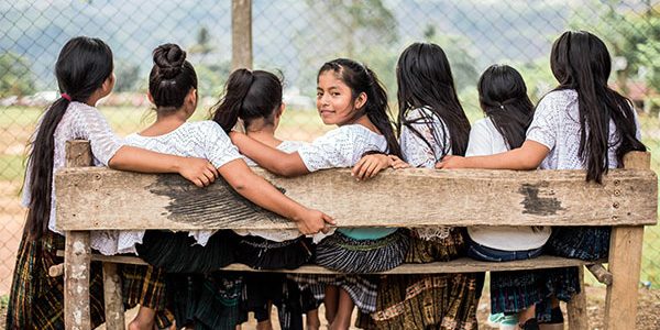 Sju flickor på rad på en bänk i Guatemala.